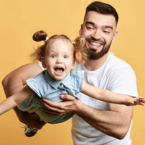 man holding up daughter like an airplane carefree from dental insurance payments