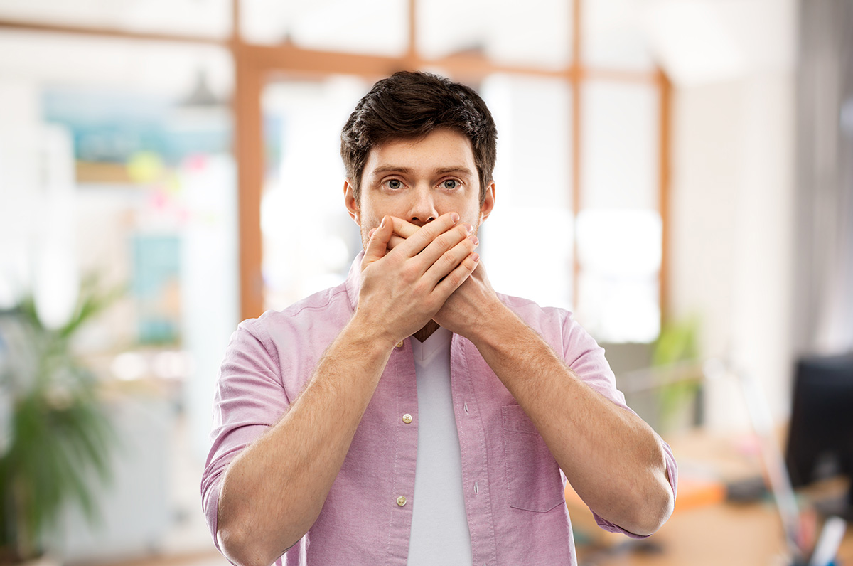 causes of bad breath (1) man covering his mouth worried about the causes of bad breath