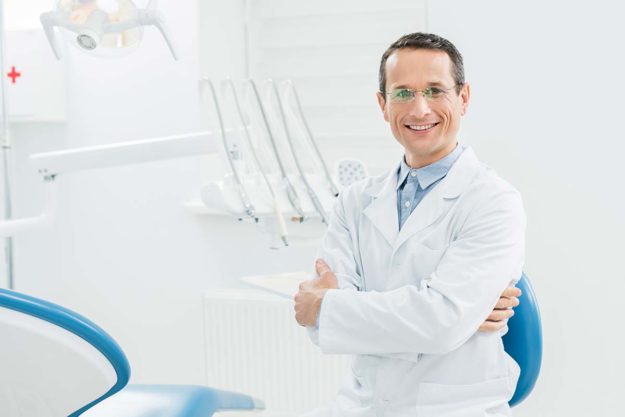 How To Choose Your Implant Dentist an implant dentist smiles in his office